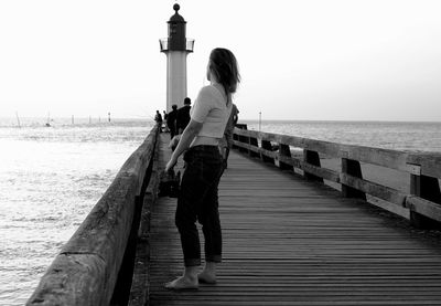 Side view of woman standing on pier against lighthouse by sea