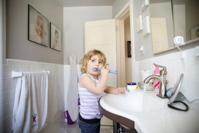 Girl looking away while brushing teeth in bathroom