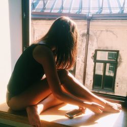 Side view of woman sitting by window