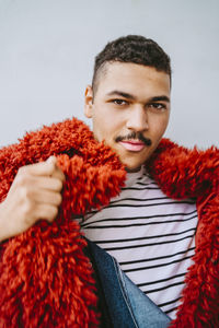 Portrait of gay man wearing red fur jacket against wall