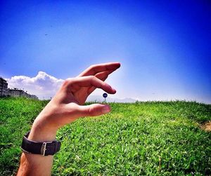 Midsection of man hand on field against blue sky