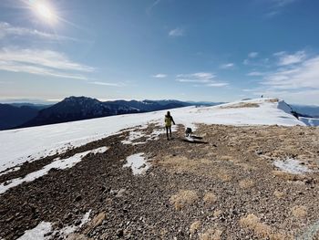 Rear view of woman walking with dog on snow covered land against sky