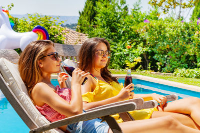 Side view of friends using mobile phone while sitting at park