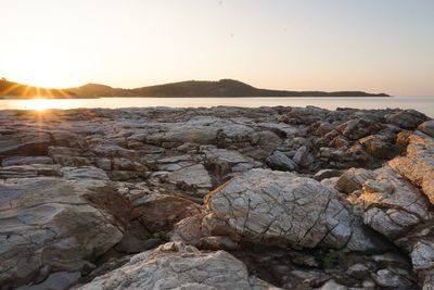 Rocks by sea against sky during sunset