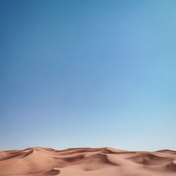 Low angle view of desert against clear blue sky