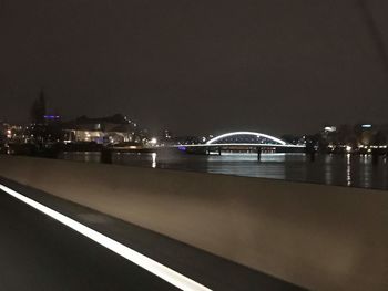 Illuminated city by sea against sky at night