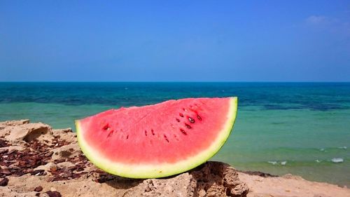 Close-up of watermelon slice on rock against blue sky