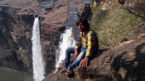 Man sitting on rock against waterfall