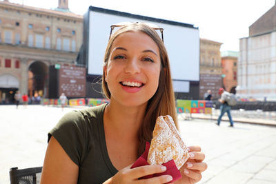 Portrait of smiling young woman holding ice cream in city
