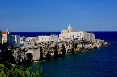 Buildings on rock formation at vieste in blue sea against sky