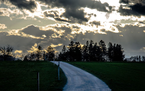 Road passing through field against cloudy sky