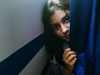 Portrait of teenage girl sitting behind curtain