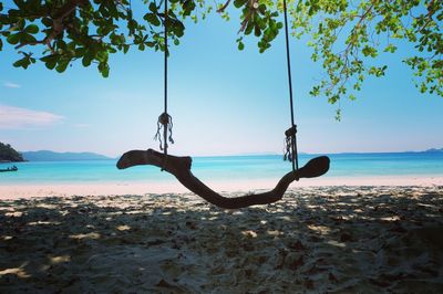 Man on swing at beach against sky