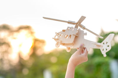 Cropped hand holding wooden toy helicopter against sky