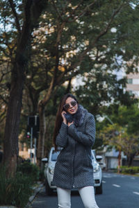Portrait of young woman standing against trees