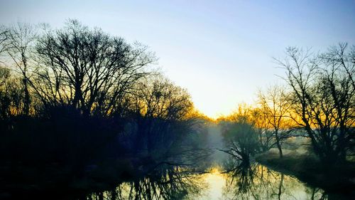 Silhouette bare trees by lake against sky during sunset