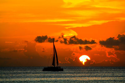 Silhouette sailboat in sea against orange sky