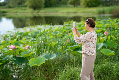 Rear view of senior woman taking a picture by lotuses lake