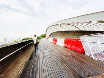 Rear view of man standing on footbridge against sky