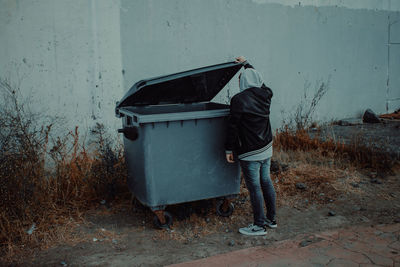 Man standing on garbage bin against wall