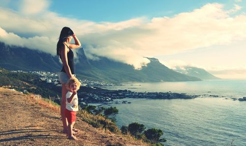 Full length of mother with daughter on hill looking at sea