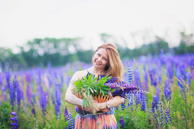 Young attractive woman holding a basket full of lupine flowers