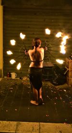 Rear view of shirtless man standing against illuminated fire