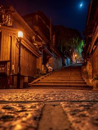 Illuminated street amidst buildings against sky at night