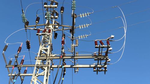 Low angle view of electricity pylon against blue sky