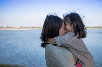 Rear view of mother and daughter at shore against sky