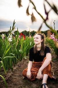 Beautiful young woman sitting on field against sky