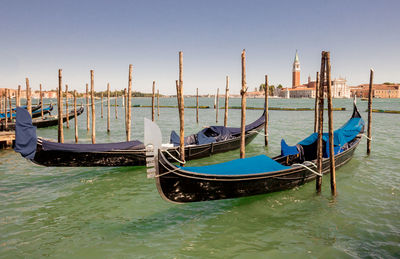 Gondolas moored in canal against clear sky