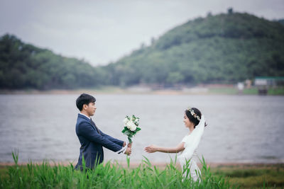 Side view of man giving bouquet to bride standing by lake