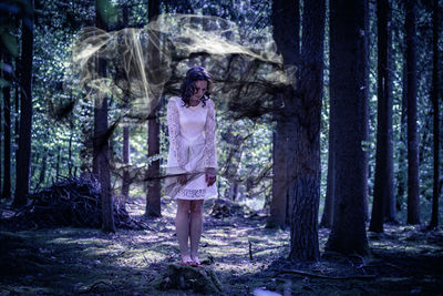 Digital composite image of woman standing amidst shawl in forest