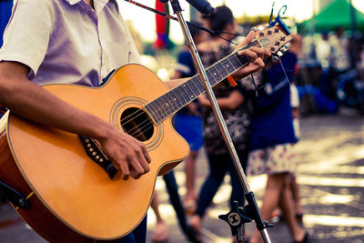 Midsection of man playing guitar on road