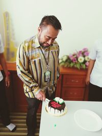 Smiling man cutting birthday cake in office