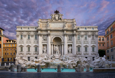 Trevi fountain against cloudy sky during sunrise in city