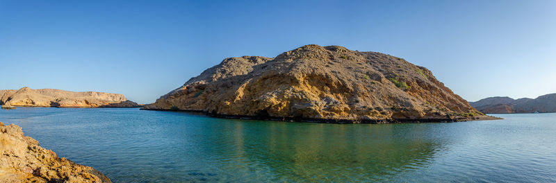 Panoramic view of sea and rocks against clear blue sky