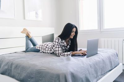Young woman using mobile phone while sitting on bed