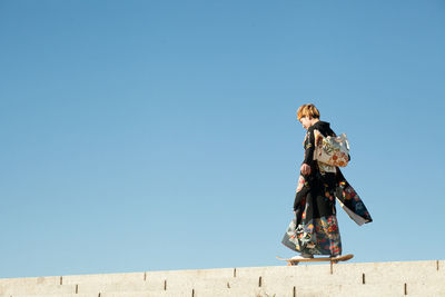 Full length side view of woman skateboarding against clear blue sky