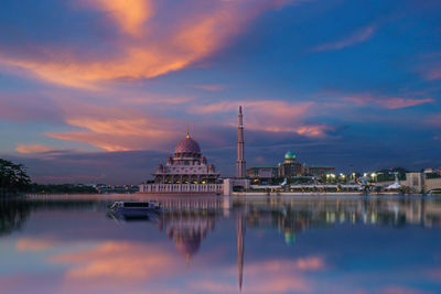 Mosque by lake against cloudy sky during sunset