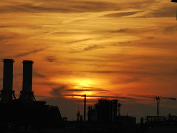 Silhouette of factory against cloudy sky during sunset