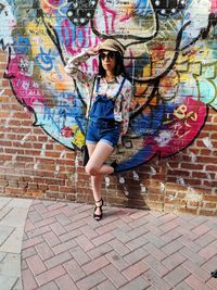 Full length of woman leaning on graffiti wall