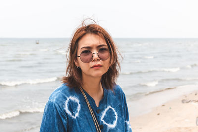 Portrait of beautiful woman standing at beach against sky