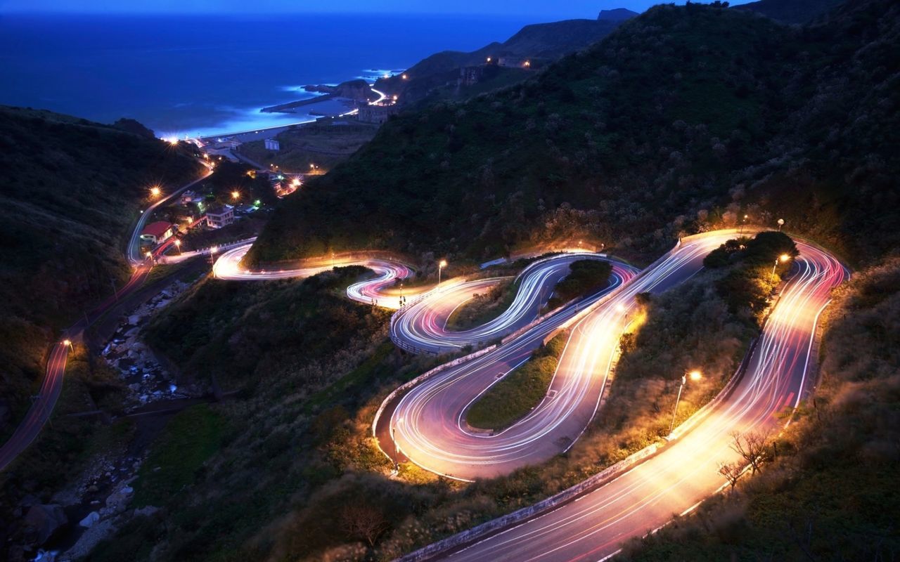 high angle view, illuminated, mountain, transportation, night, sky, road, scenics, landscape, nature, long exposure, tranquil scene, outdoors, water, no people, beauty in nature, motion, tranquility, aerial view, light trail