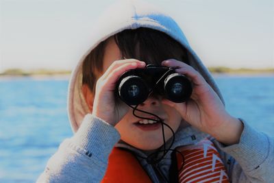 Close-up of boy looking through binoculars while standing against lake