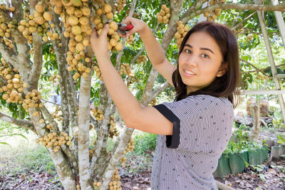 Portrait of young woman standing by tree against plants