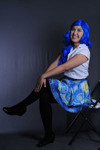 Portrait of young woman sitting against wall