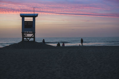 People on beach against sky during sunset