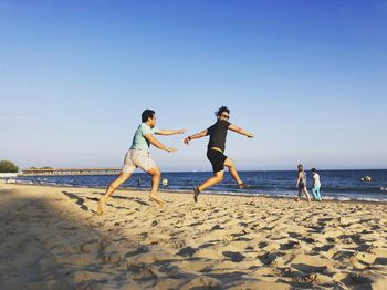 Friends playing at beach against clear sky